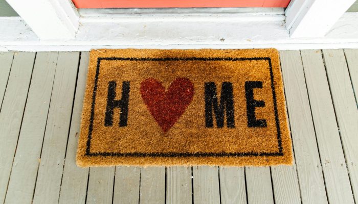 Doormat with 'Home' written and heart symbol on wooden porch.